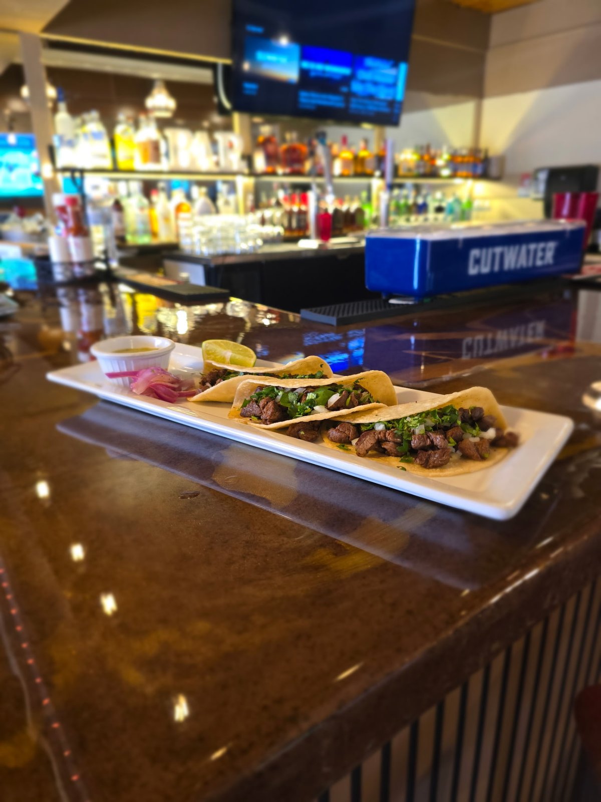 Three steak street tacos with cilantro and onion on a white plate with salsa, lime and pickled onions
